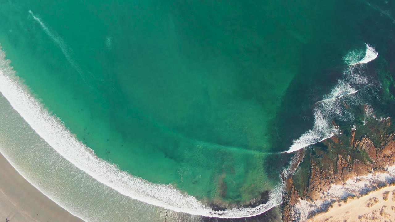 Aerial view of white wave foam nearing a rocky point