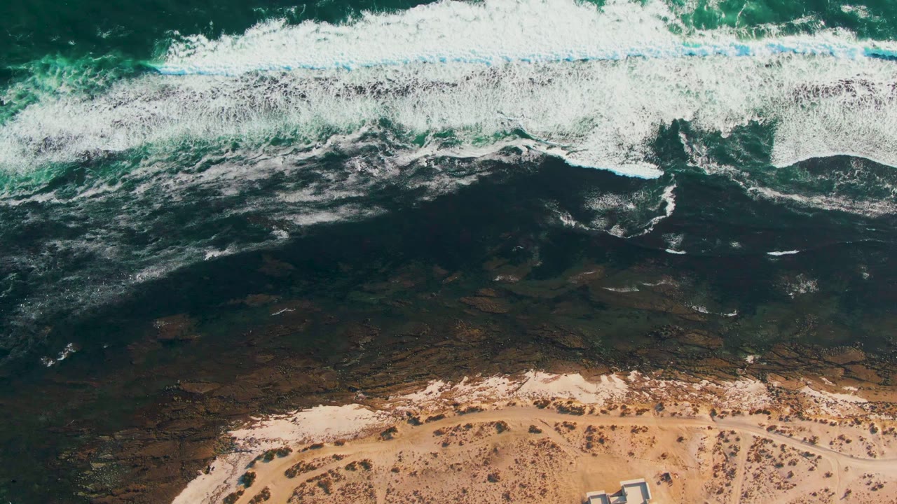 Foamy waves crossing dark shallow water near sand