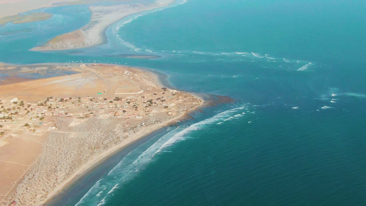 High aerial coastline with settlement, sandy beach, inlet, and blue water.