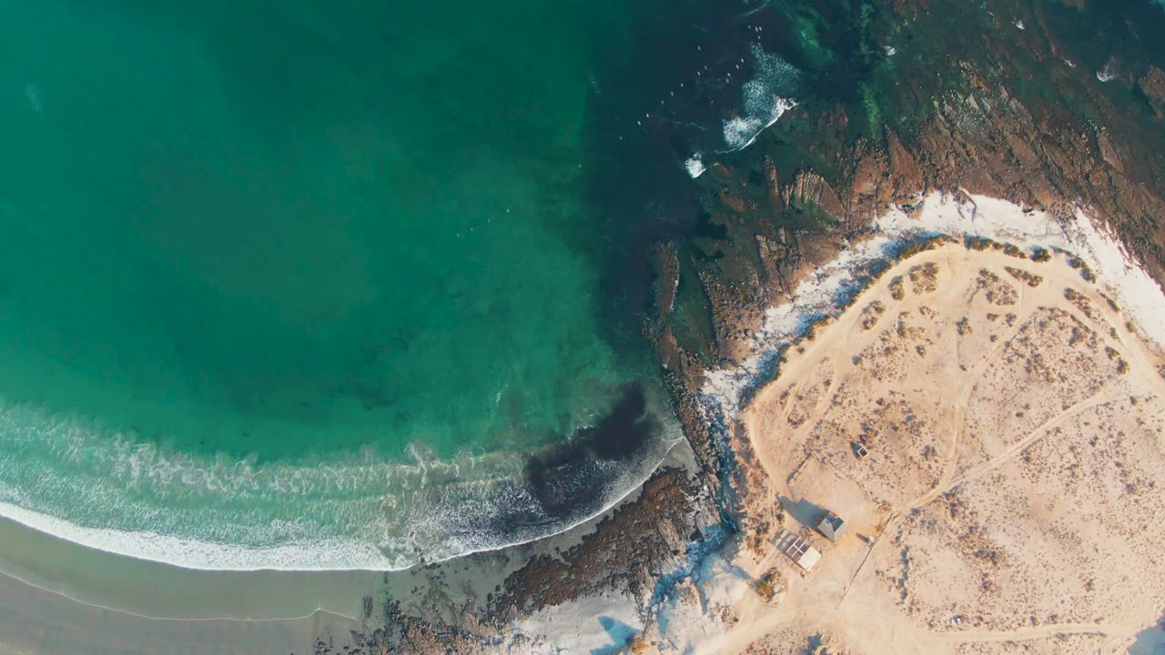 Aerial shoreline with waves meeting sand beside dark rocks