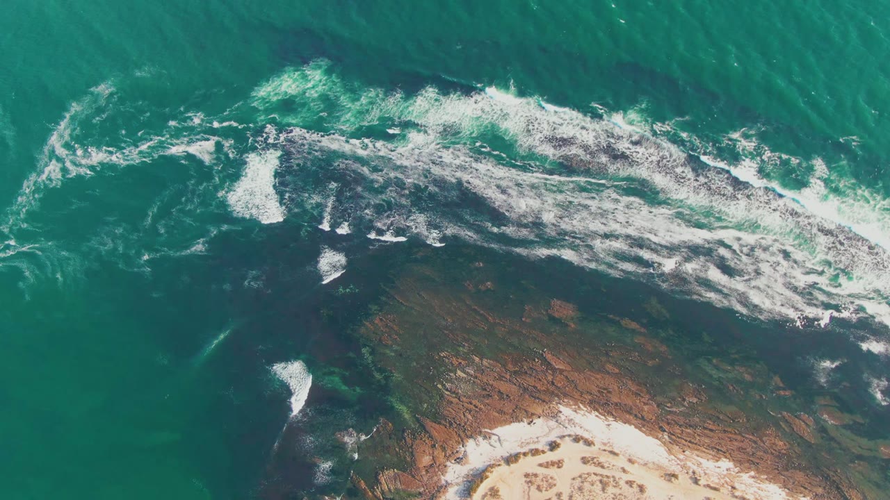 Whitewater spreading over dark rocks beside turquoise water