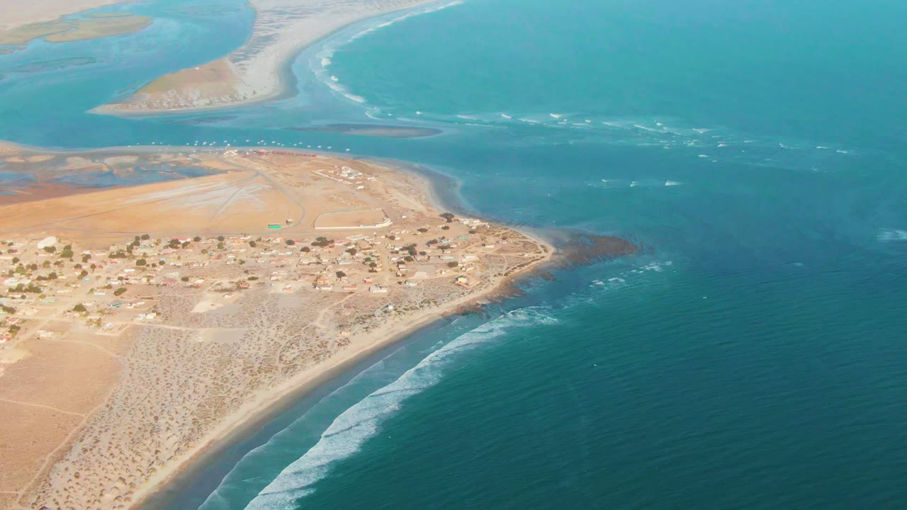 Wide drone view of settlement, beach, and surf lines