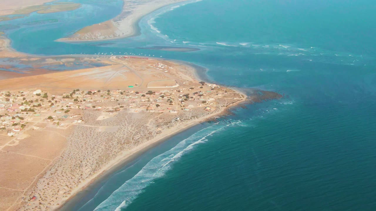 Aerial coastline with scattered village buildings and breaking waves.