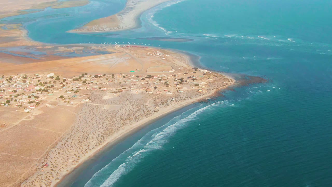 High coastal view of houses, dry land, beach, and blue water.