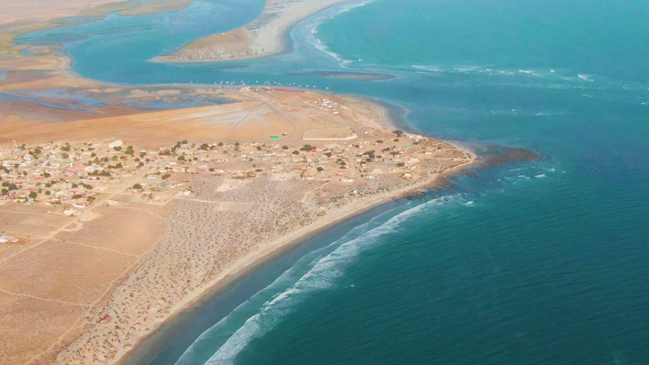La Bocana aerial view showing the village on a sandy coastal point, darker reef or rock patches near shore, bright water beyond, and no visible people.