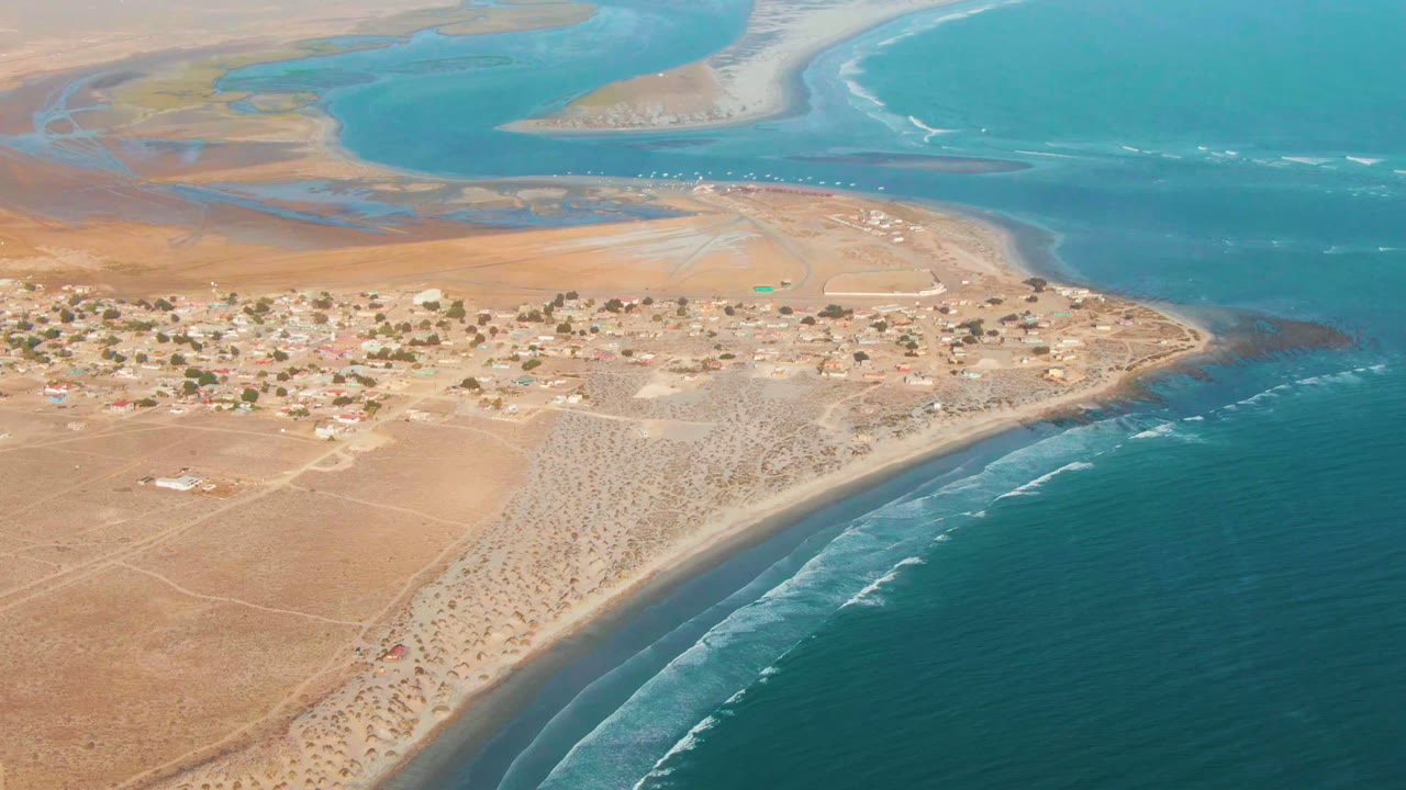 Drone view of a sandy settlement between desert land and ocean waves
