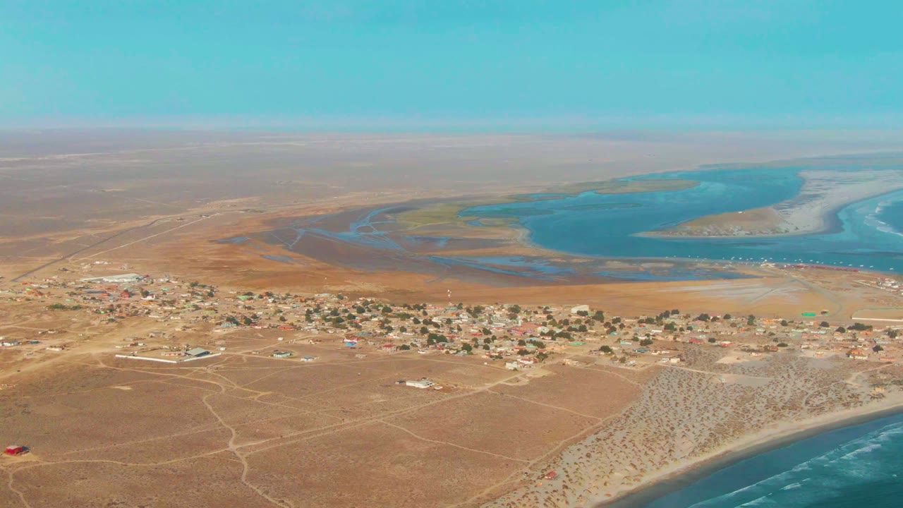 Wide aerial view of dry settlement with lagoon and coastline