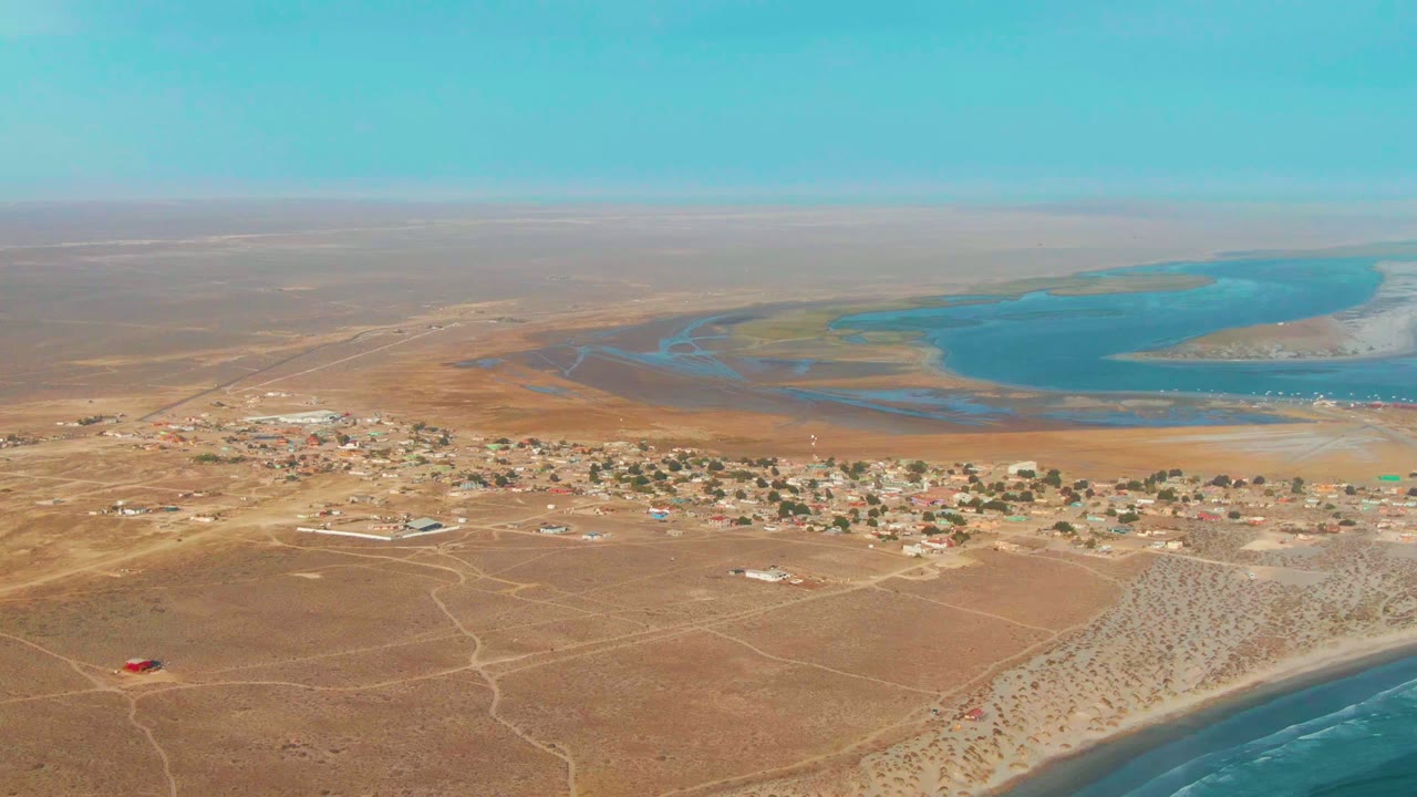 Wide aerial view of sandy roads, scattered houses, lagoon, and coastline