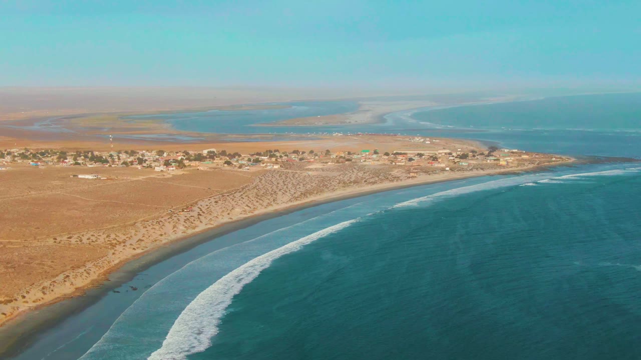 At 0:02, La Bocana's beach arcs across the frame as a long white foam line moves along the near shore, with desert flats and no visible people inland.