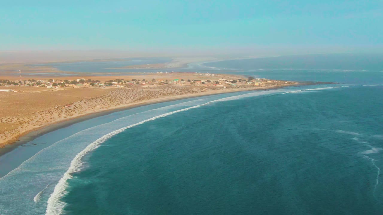Aerial coastline view with white surf curling toward a sandy beach.