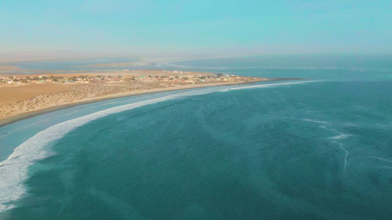 White surf spreads along a sandy shoreline beside turquoise water.