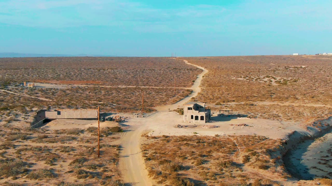 Dirt road curves through dry desert toward small abandoned buildings.