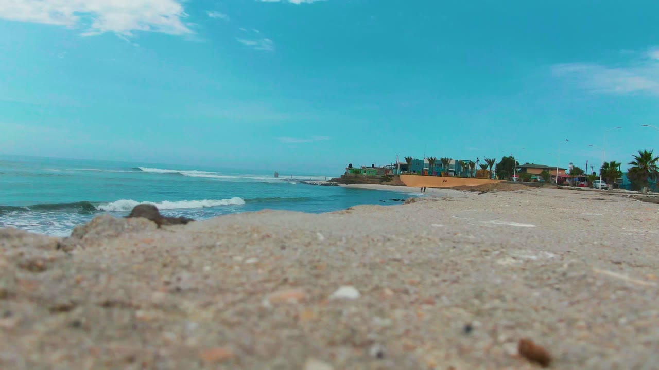 Beach sand foreground with surf rolling toward a distant coastal edge.