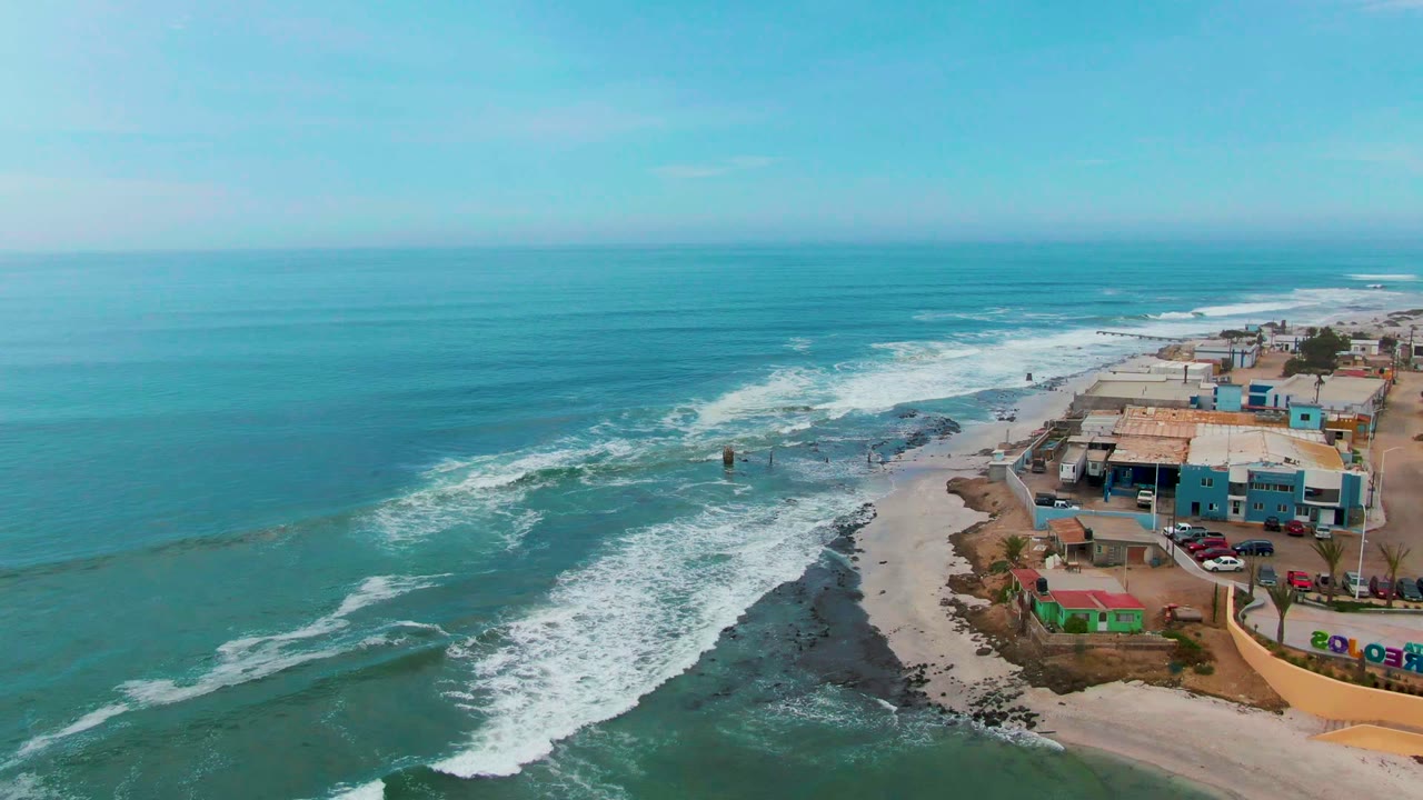 Ocean surf spreads across a rocky shoreline next to beach buildings.