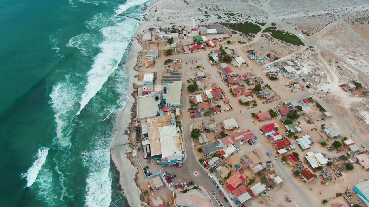 Ocean foam moves along the shore next to roads and low buildings.