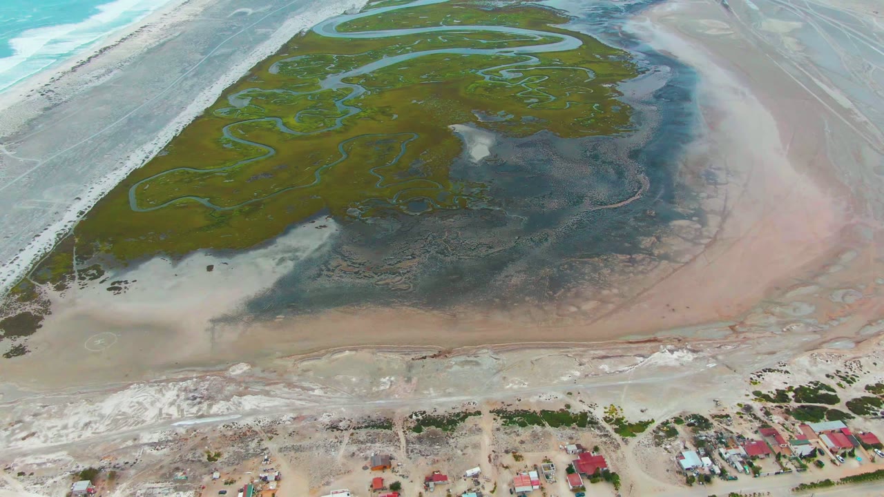 Overhead coastal wetland with winding channels and houses near the lower shoreline.