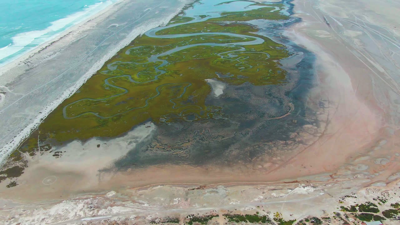 Drone view of coastal lagoon water channels with ocean surf along the left edge.
