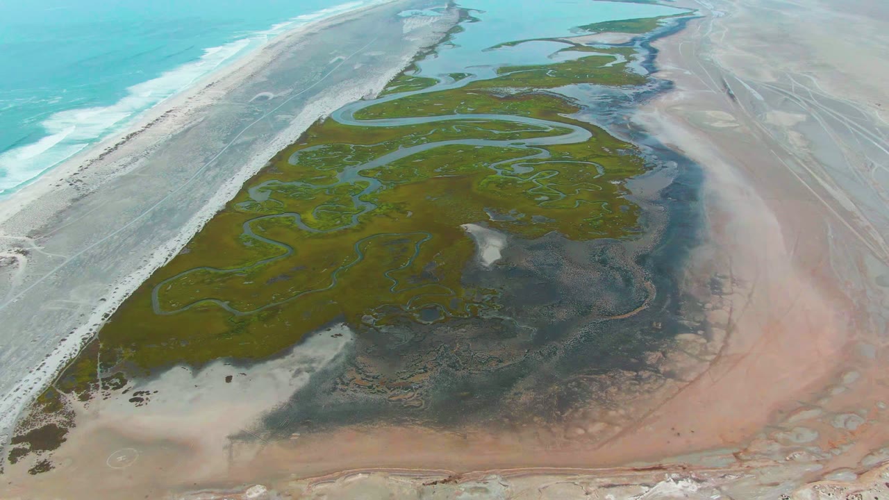 Aerial coastline view with lagoon channels between beach and broad wet sand flats.