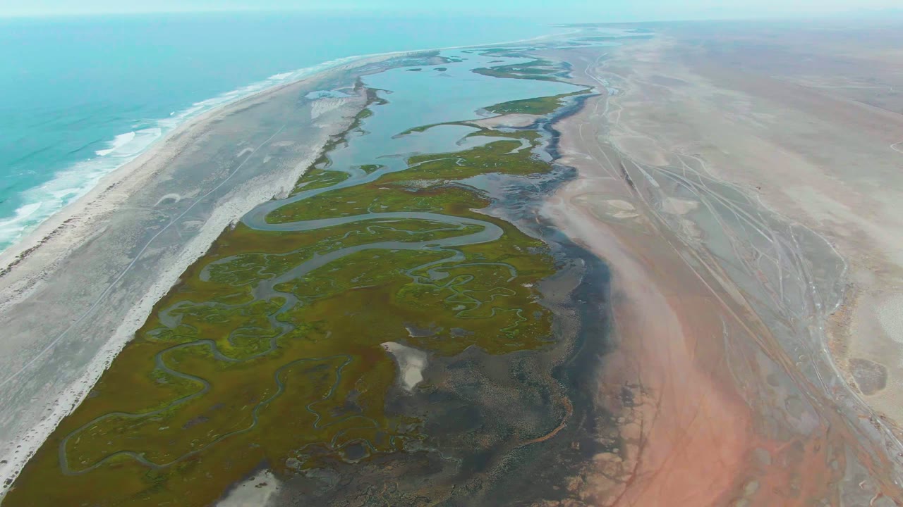 High aerial coastline view with winding tidal channels and beach surf.