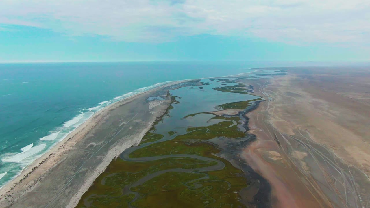 Drone view of turquoise ocean beside a beach and winding wetland channels.