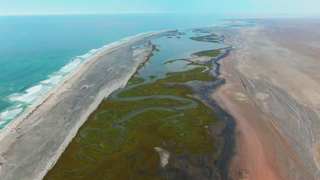 Coastal wetland channels between surf beach and reddish arid land.