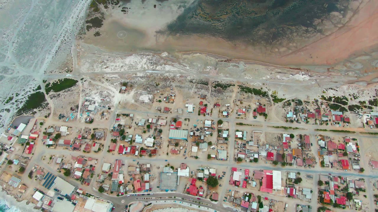 Aerial village blocks with surf below and tidal water above.
