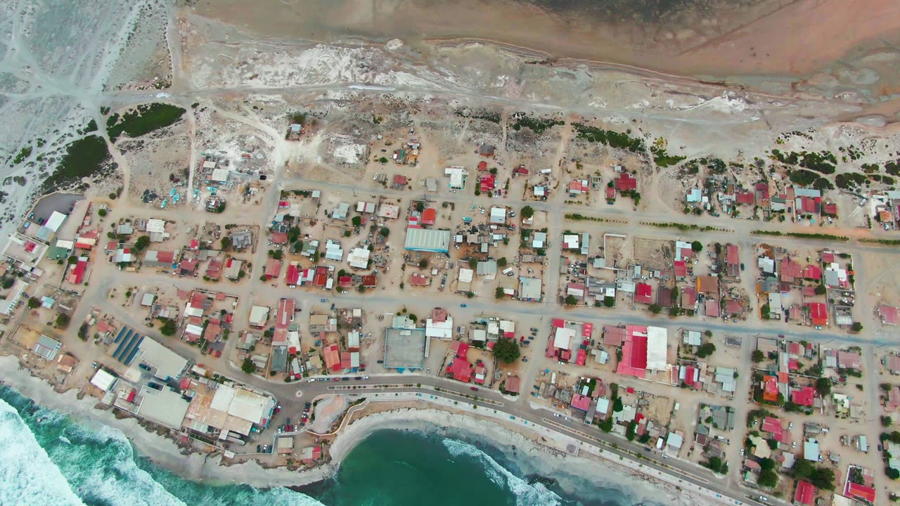 Aerial view of village roads and white surf along the shore.