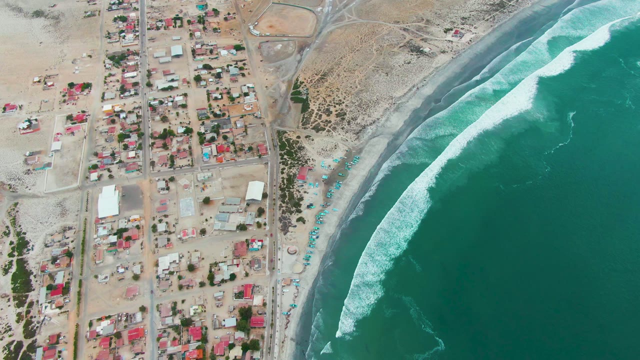 Aerial shoreline with houses, beach edge, and white wave line.