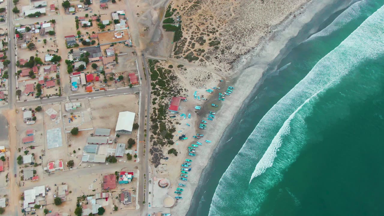 Aerial view of houses, beach line, blue umbrellas or boats, and surf