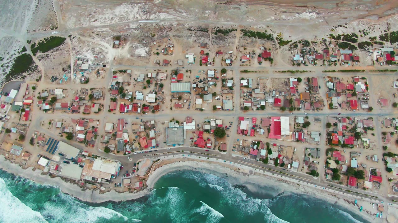 Aerial view of houses, roads, dry terrain, and surf.