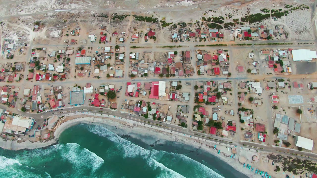 Aerial view of houses and a curved beach with surf.