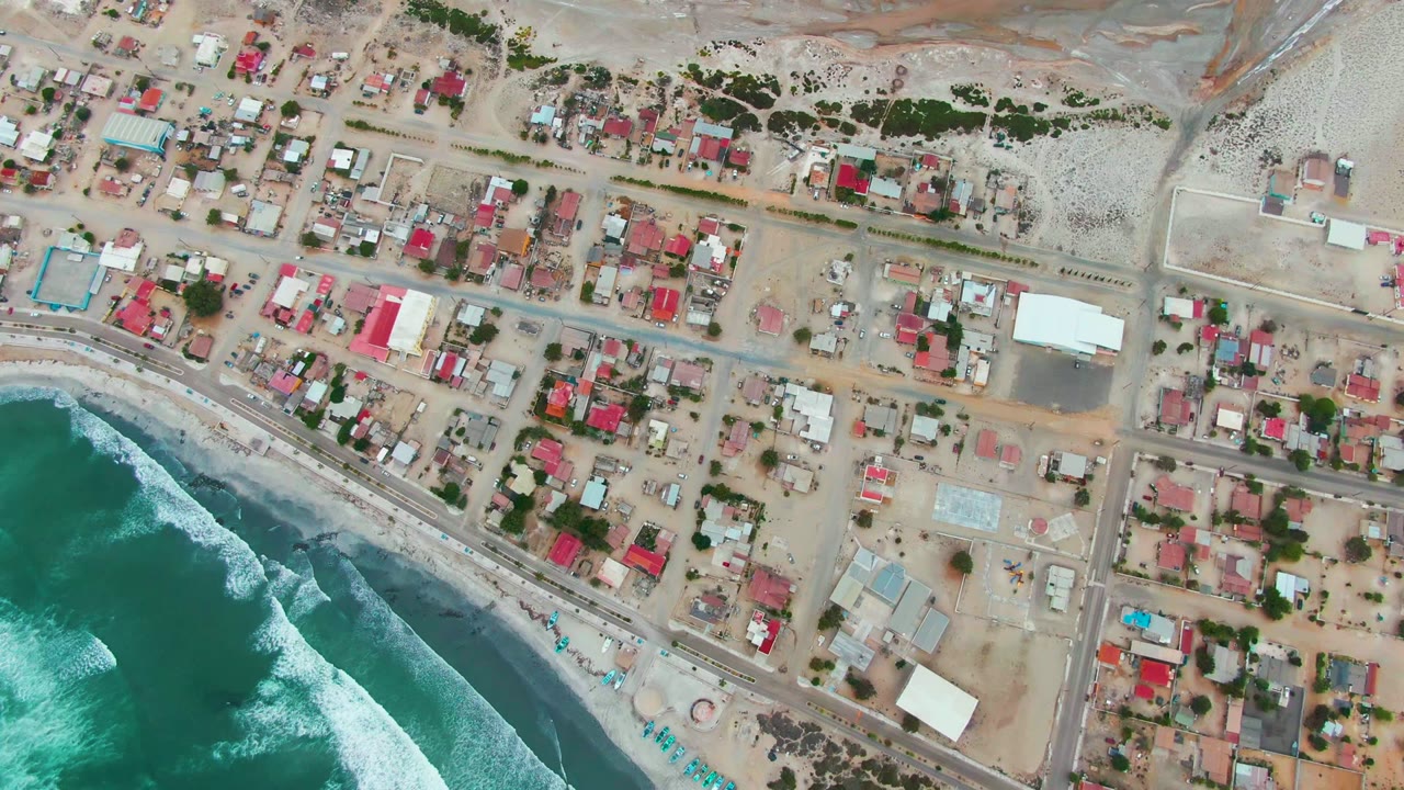 Aerial view of waves, beach road, and gridded houses near the coast.