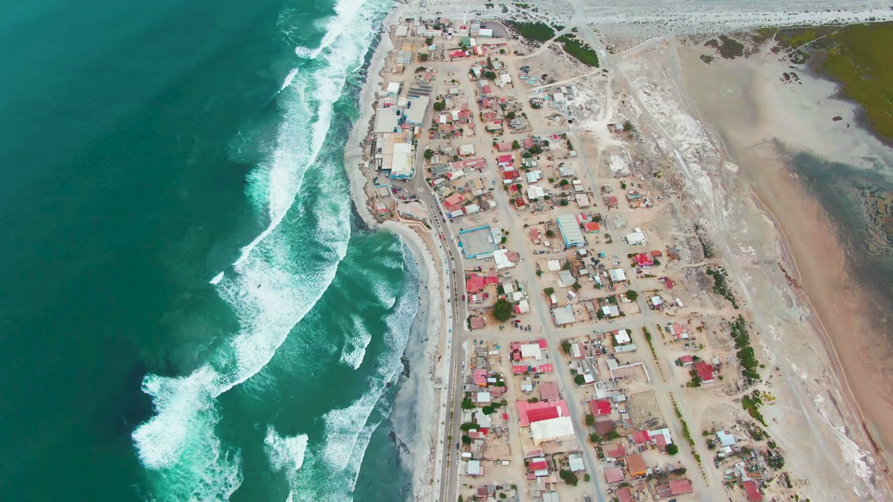 Aerial coastal village with white waves curling along the shoreline.