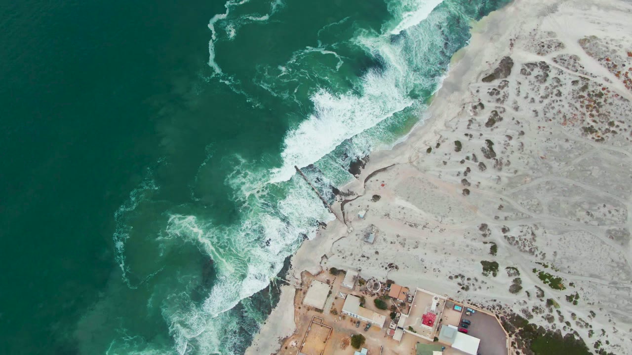 Turquoise water and white waves along pale beach with buildings below