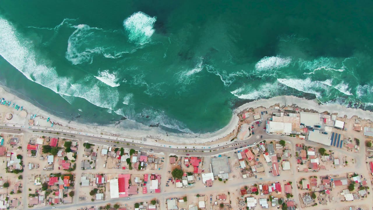 White wave foam breaks offshore above a road and town blocks.