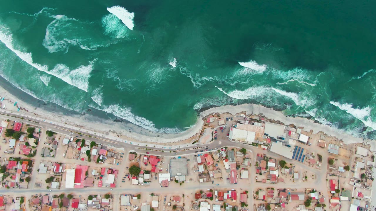 Aerial shoreline with foamy waves and red-roofed town blocks.