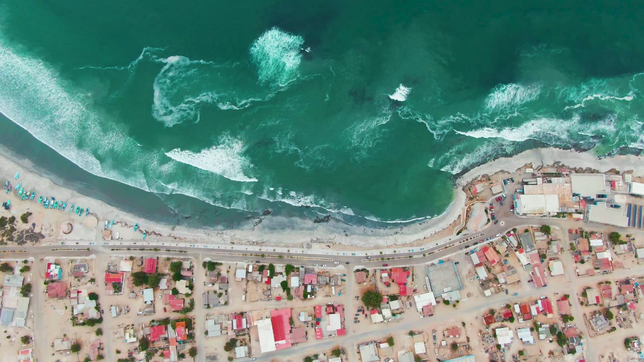 Aerial view of waves breaking beside a beach road and homes.