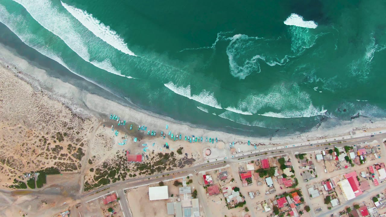 Aerial view of waves, beach umbrellas, road, and coastal town.