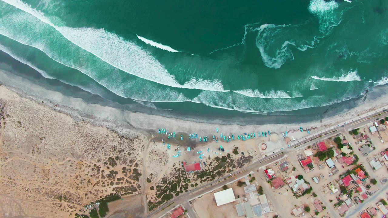 Aerial shoreline with breaking waves and a small coastal settlement.