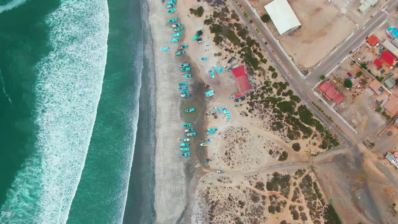 Breaking waves beside beach with blue boats and inland roads