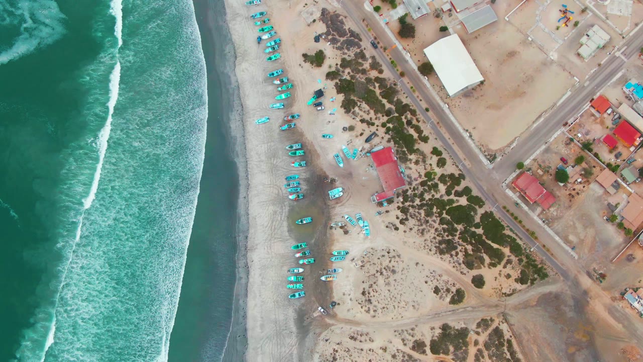 White surf line beside sandy beach with blue gear and inland roads