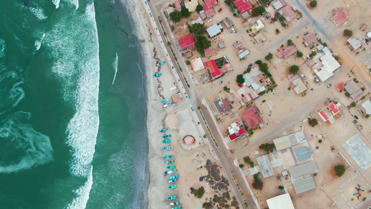 Aerial beach town edge with waves, road, clustered homes, and small boats.
