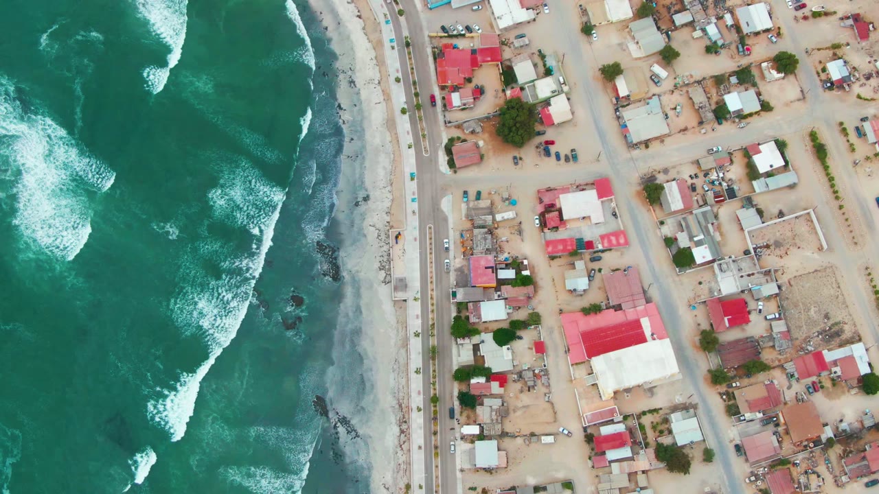 Aerial beach town blocks beside foaming ocean waves.