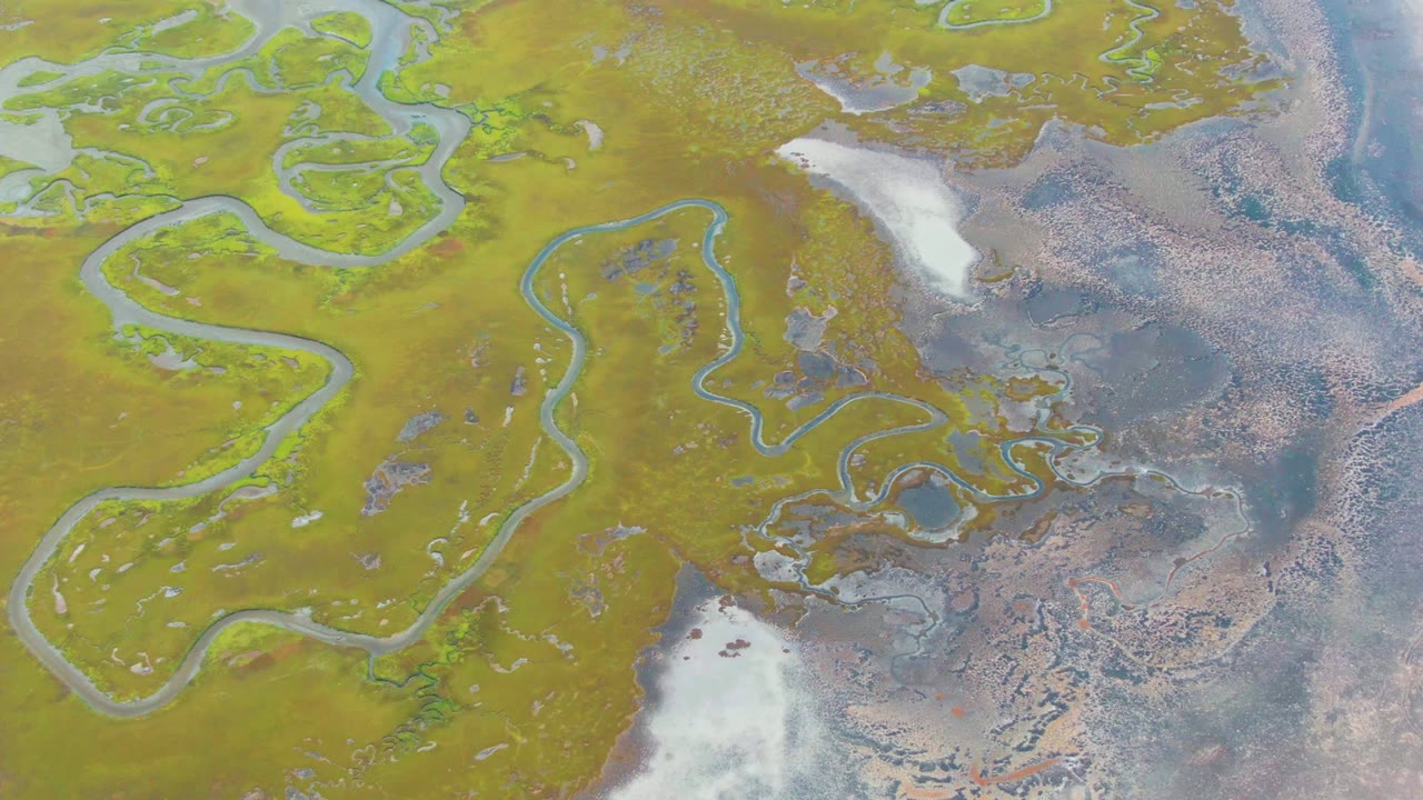 Aerial view of meandering water channels, wet flats, and bright white ice patches.