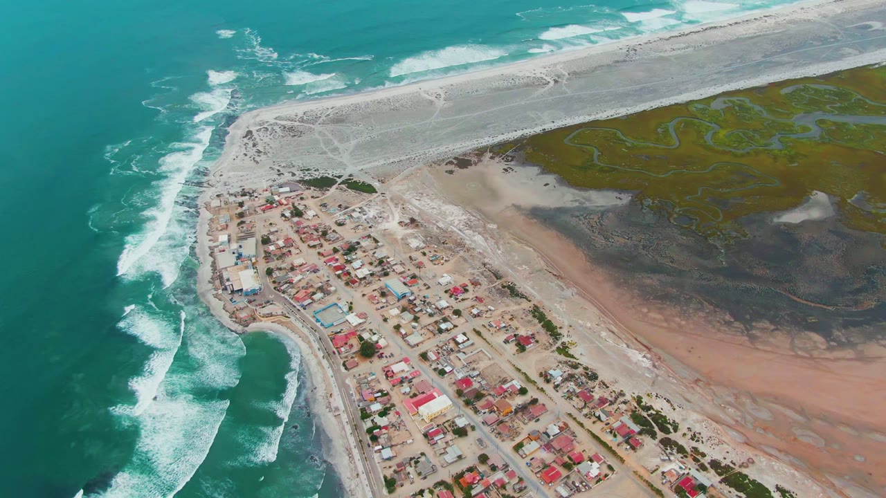 Drone view of waves beside a small town and tidal wetlands.