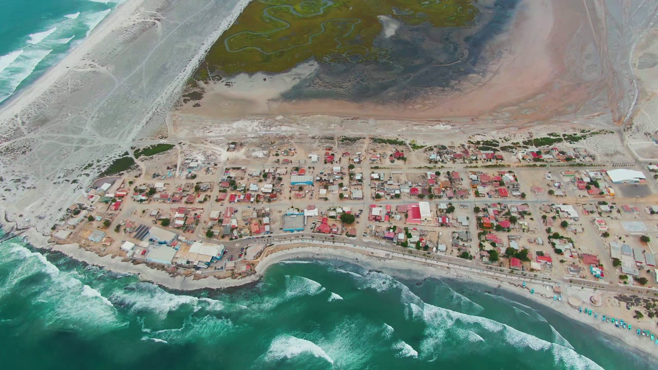 Aerial view of sandy settlement with ocean waves and exposed lagoon shore.