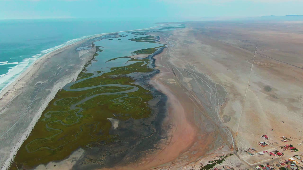 Drone view of wetland channels beside ocean surf and sandy flats.