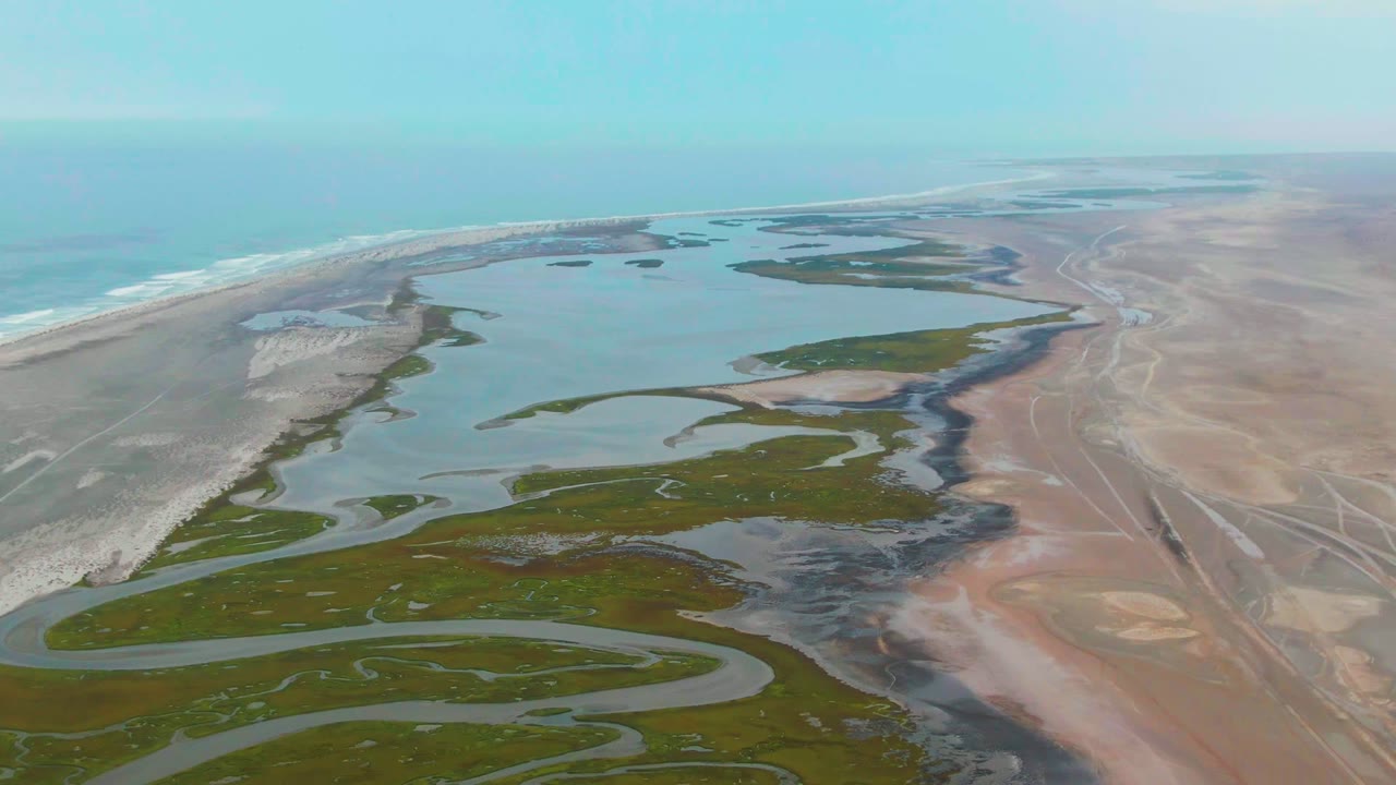 At 0:02, the drone perspective shows the ocean along the left horizon, a sandy coastal strip, green delta patches, tan flats, and no visible people.