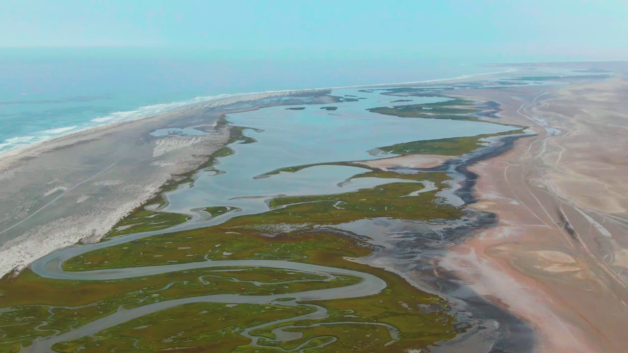 At 0:00, an aerial view over Punta Abreojos shows turquoise ocean surf, a pale sand barrier, green wetland islands, winding river channels, and no visible people.