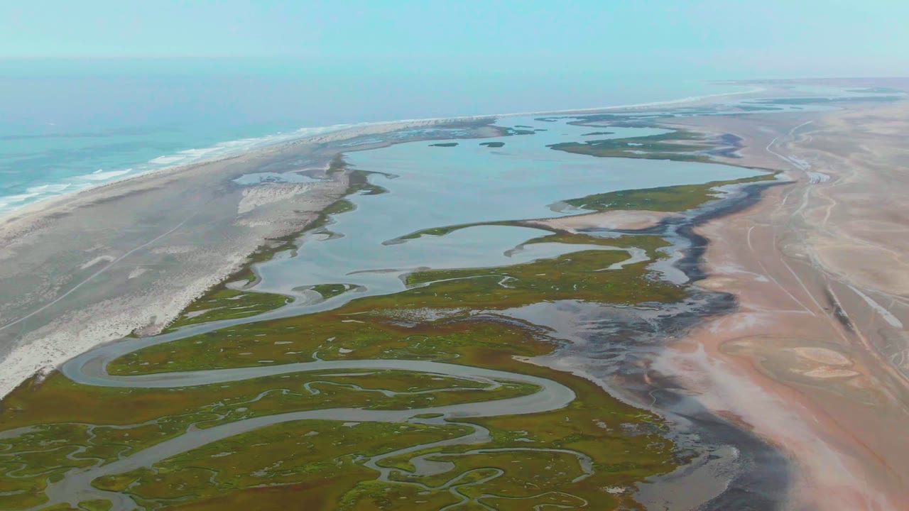 At 0:02, Punta Abreojos wetland pools and marsh patches fill the lower frame while a long sand spit separates the lagoons from the ocean, with no visible people.